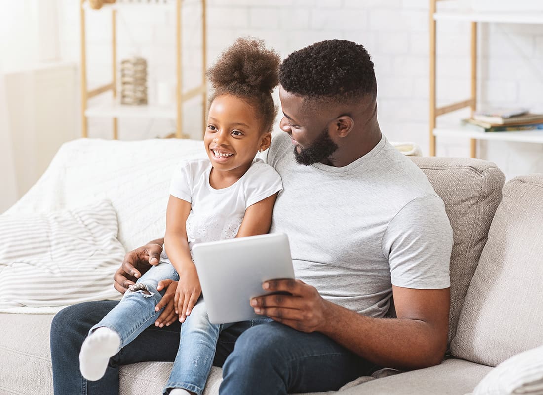 Insurance Solutions - Happy Father and Daughter Sit Together Using a Tablet at Home